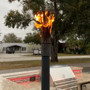 A torch with a flame burning atop a pole in an outdoor park setting.