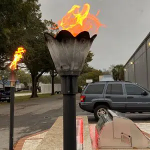 Torch with bright flame outdoors near parked cars on a cloudy day.